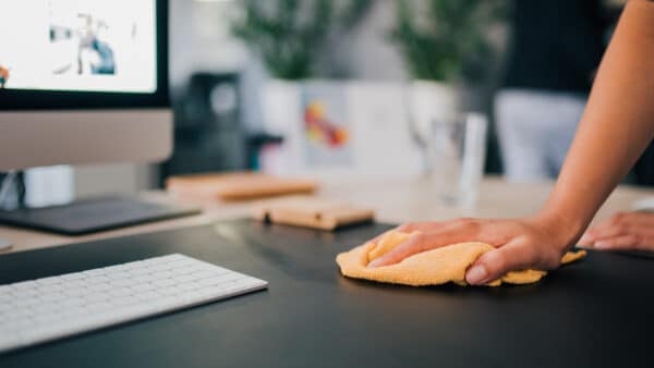 A hand wiping an office desk with a yellow cloth