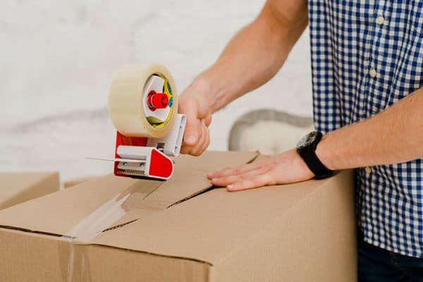 a man holding a tape dispenser while wrapping it on a box