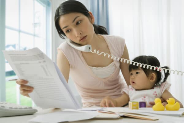 A busy mother talking on the phone while carrying her baby