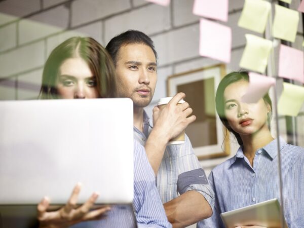 a team of asian business people conducting a SWOT analysis in office using laptop computer and sticky notes