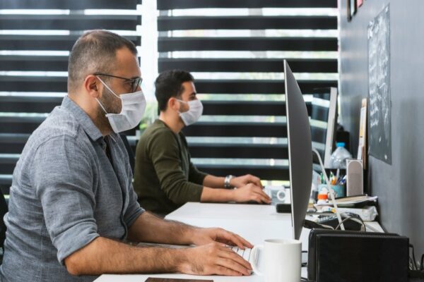 two men wearing face masks working on their desks