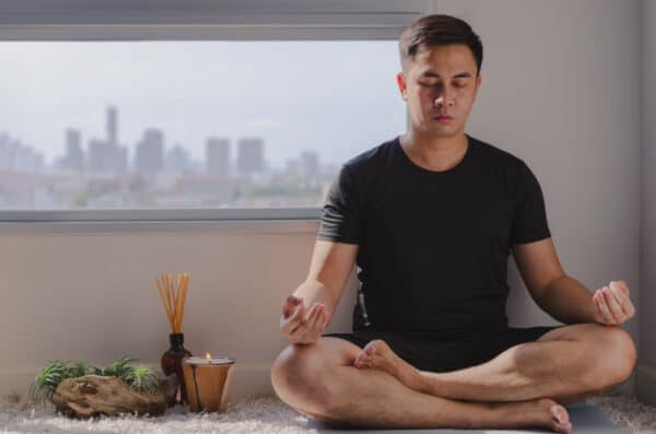 an asian man meditating beside his apartment window