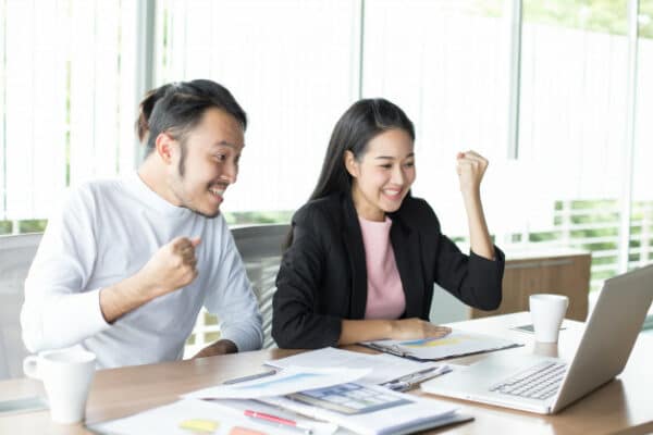Two workers excitedly looking at the laptop screen