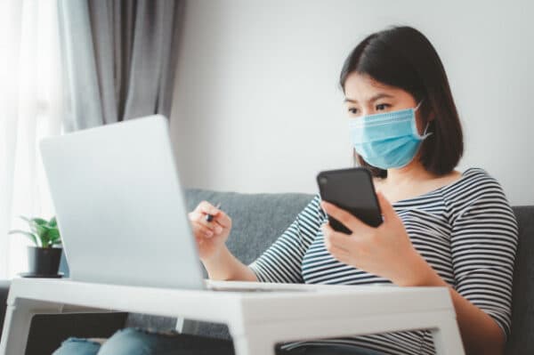 an asian woman wearing a face mask while working from her in her living room