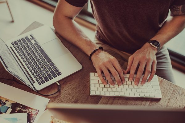 a man in a brown wearing a wrist watch shirt typing on his keyboard