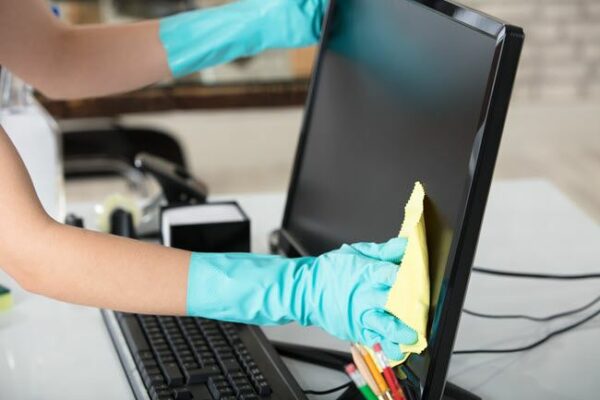 a person wearing gloves wiping a computer monitor with cloth