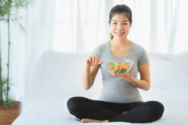 a happy asian woman sitting on her sofa while having a healthy meal