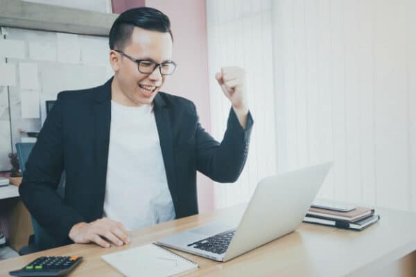 a happy young asian businessman looking at his laptop