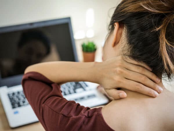 A woman touching her painful neck while fronting a laptop