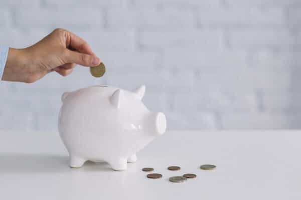 A hand putting a coin inside a porcelain piggy bank