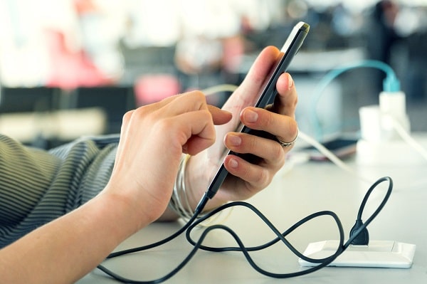 A hand using a mobile phone while charging it in public