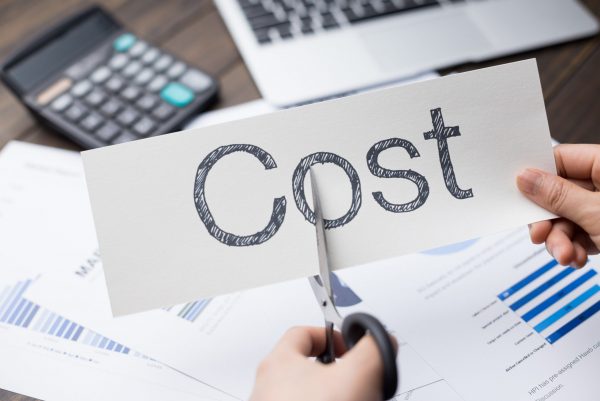 a person cutting a piece of paper with the word cost written on it