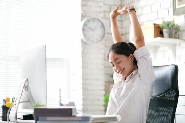 an asian woman stretching at her desk