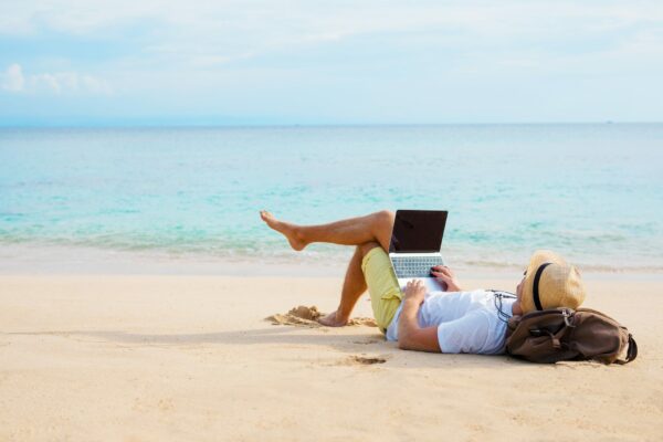 A man relaxing at the beach while working on his laptop