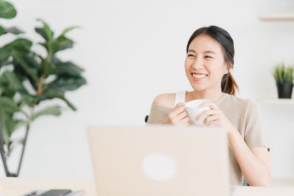 A happy woman drinking coffee while working from home